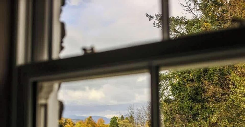 Capture the essence of Fair Rigg's Ruskin suite with an great view through the original wooden sash window, framing the serene beauty of the distant lake and fells. A unique blend of heritage and natural splendor awaits you