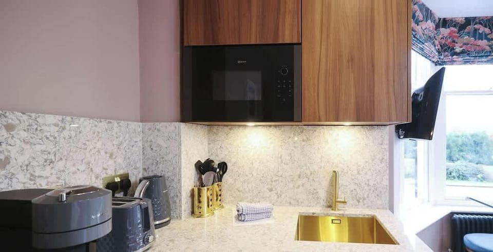 The Ruskin Studio @ Fair Rigg showcases a sleek kitchenette with a Neff Combination oven, brushed brass accents, and a Nespresso machine for a touch of modern convenience.