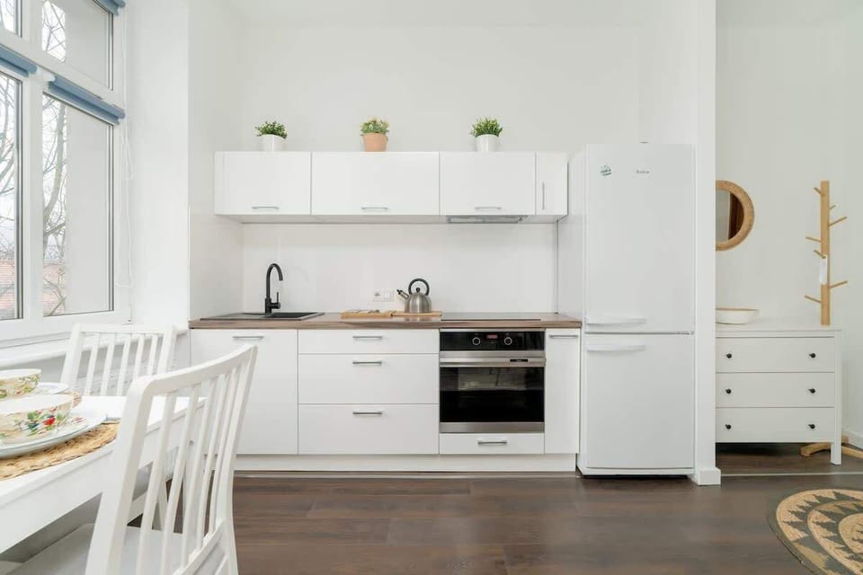 A modern, all-white kitchen with open shelving, built-in appliances, and a sleek design, blending functionality with aesthetic appeal.

