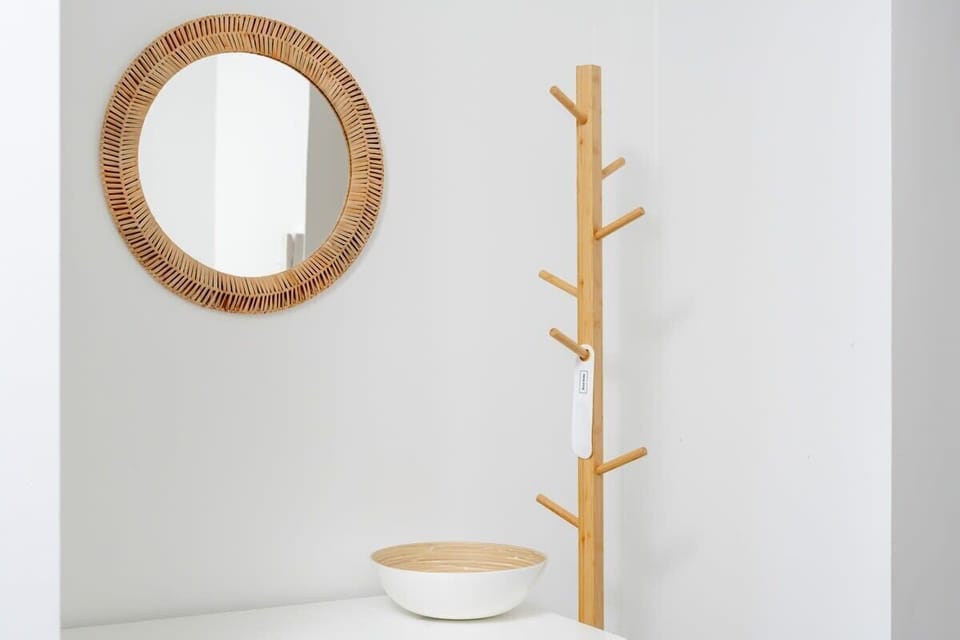 A minimalist entryway featuring a round woven mirror and a modern wooden coat rack.

