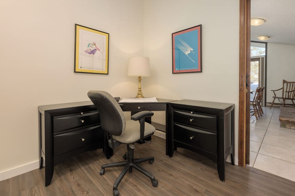 Your dedicated workspace awaits with a spacious L-shaped desk, ergonomic chair, and warm lighting for productive days.