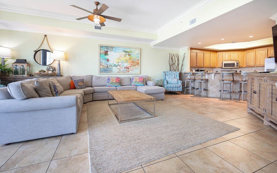 The living area features a cozy sectional sofa, colorful accents, and a view into the modern kitchen with bar seating