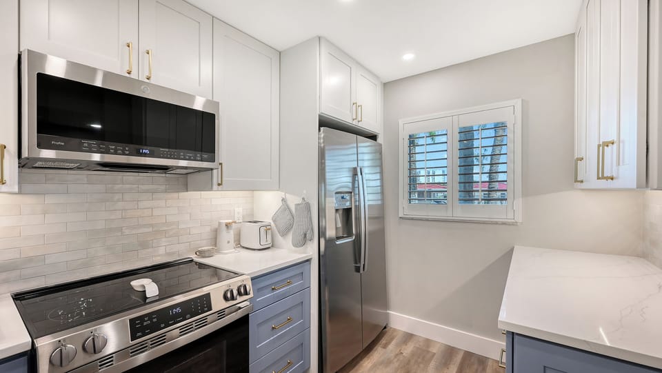 Prepare your favorite meals in this bright, modern kitchen featuring stainless steel appliances, sleek white cabinetry, elegant gold hardware, and plenty of counter space for your culinary adventures.