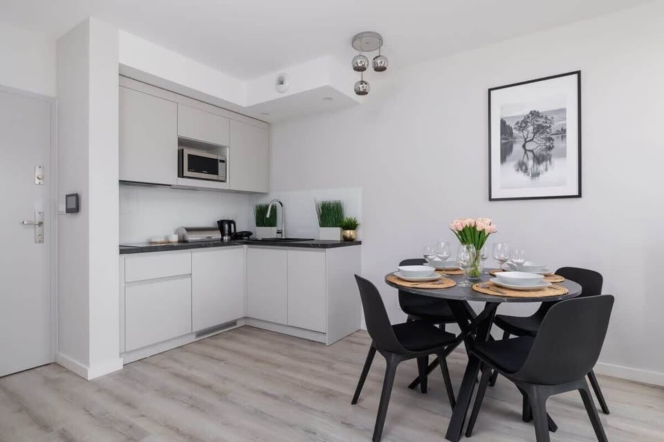 A bright open-plan dining and kitchen area with a minimalist design, white walls, and black furniture for a sleek contrast.

