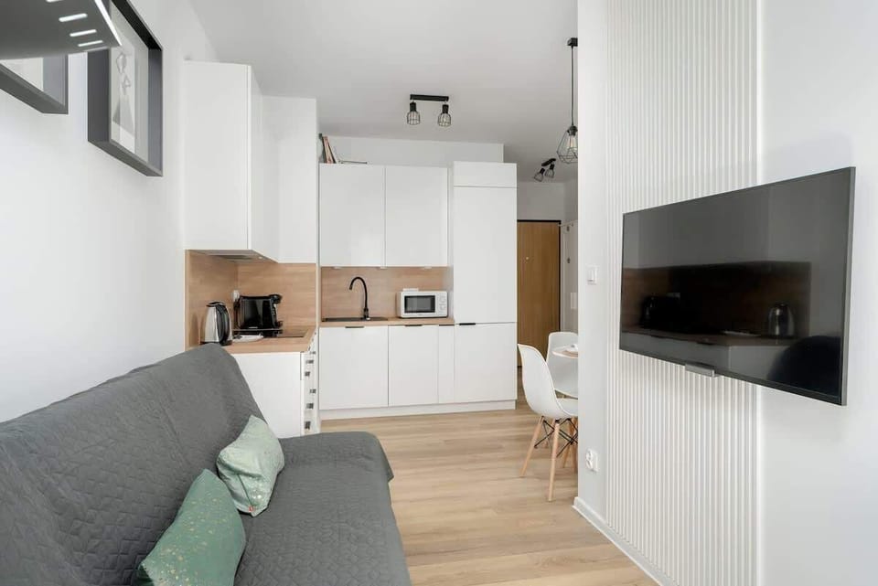 A sleek, contemporary apartment interior with an open-plan living space, featuring a gray couch, a mounted TV, and a functional kitchen.

