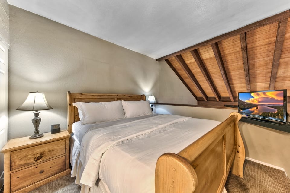 Unwind in your lofted bedroom featuring rustic wood furnishings, exposed beam ceiling, and all the comforts for a perfect mountain retreat.