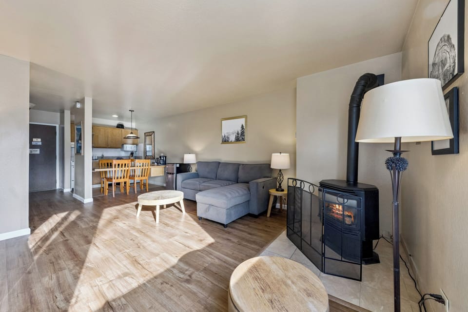 Unwind in your open-concept living space featuring a cozy fireplace, modern kitchen, and comfortable sectional sofa perfect for mountain evenings.