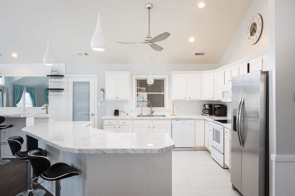 Top Level: Bright open kitchen with large island bar seating for five, stainless steel appliances, coffee maker, and a fully stocked layout perfect for gathering and entertaining.