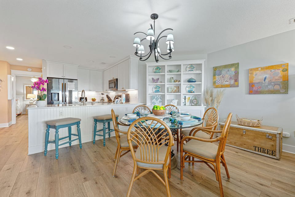 This light-filled dining area offers a comfortable gathering space with seating for six, set beneath a classic chandelier that adds a warm coastal touch.