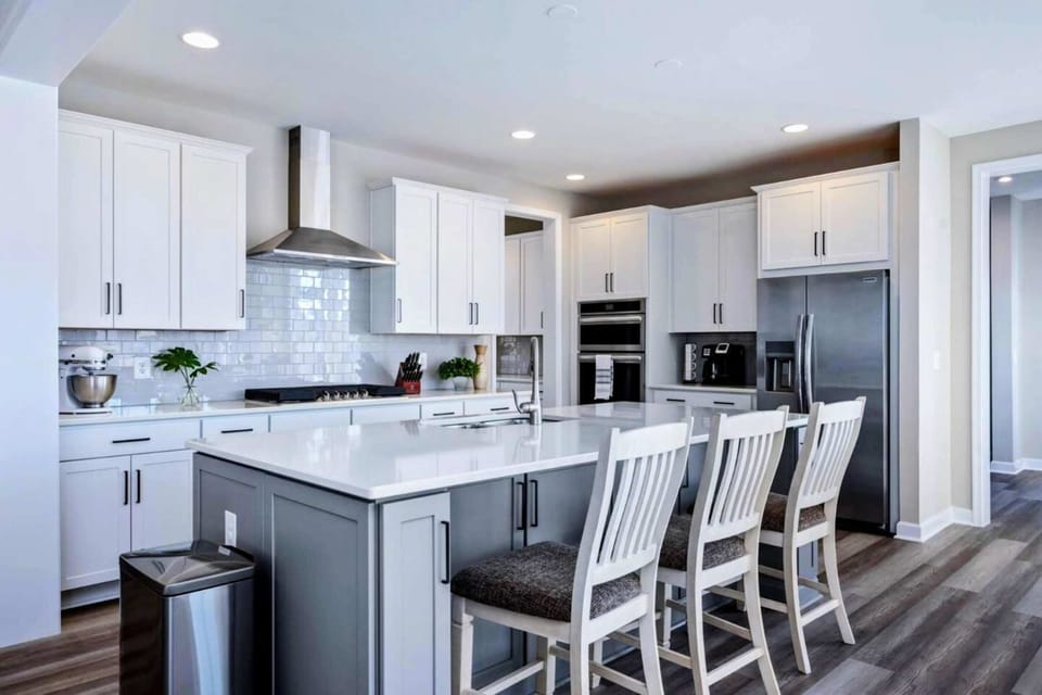 Chef's Kitchen - Wide white island, gas cooktop with stainless hood, and counter seating for casual meals or pre-dinner drinks.
