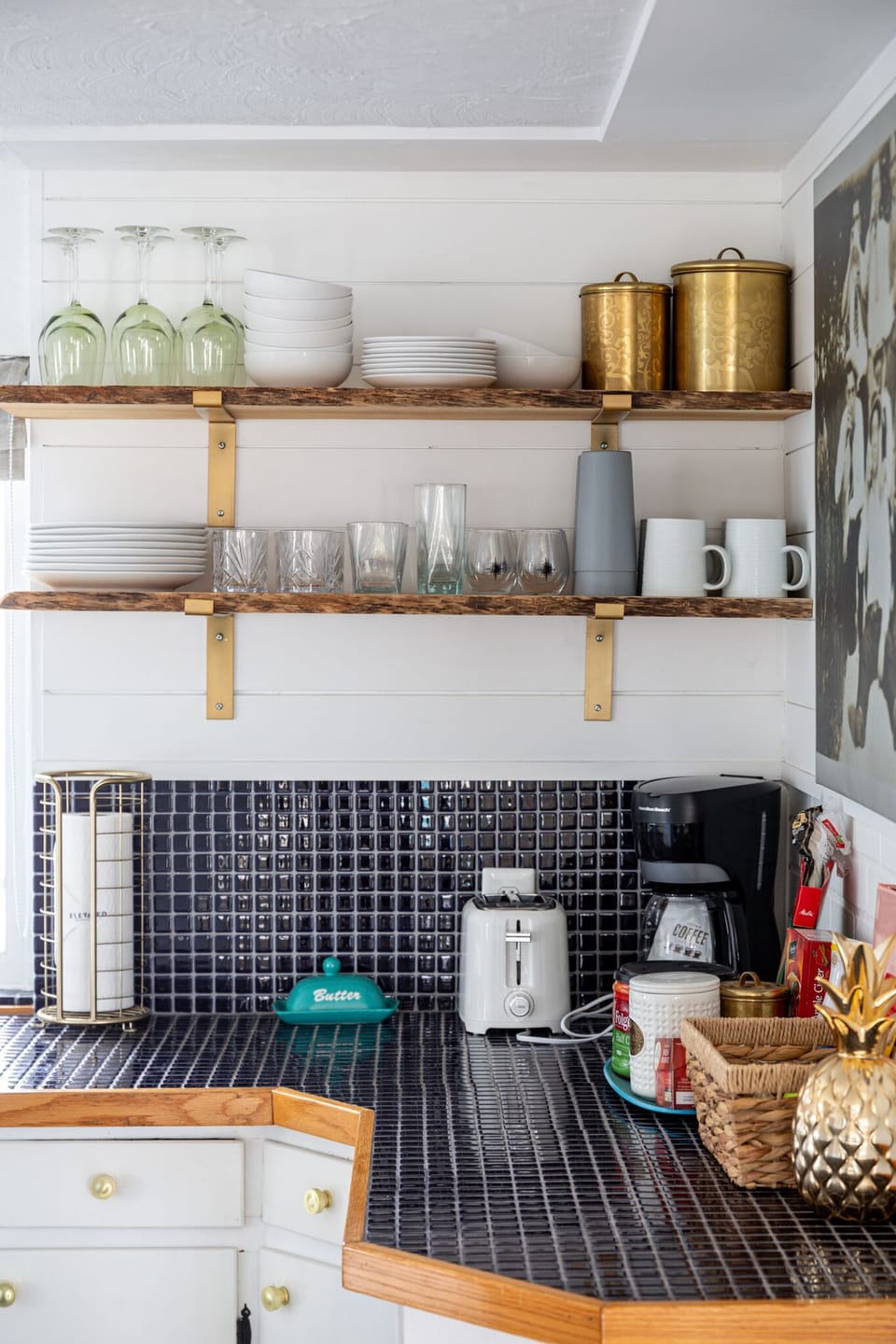 Open kitchen shelving w/ dishes & glassware neatly displayed above a tiled backsplash.