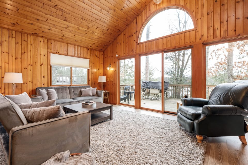 Bright living room w/ vaulted wood ceilings, plush seating & large arched windows overlooking the lake.