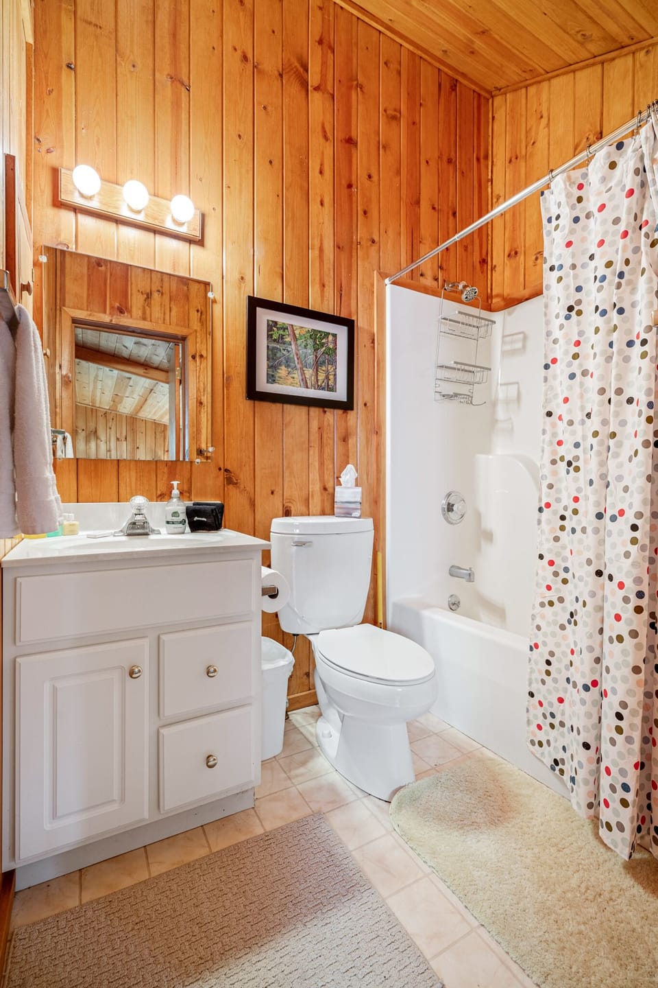 Full bathroom w/ wood walls, vanity sink & shower-tub combo w/ colorful curtain.