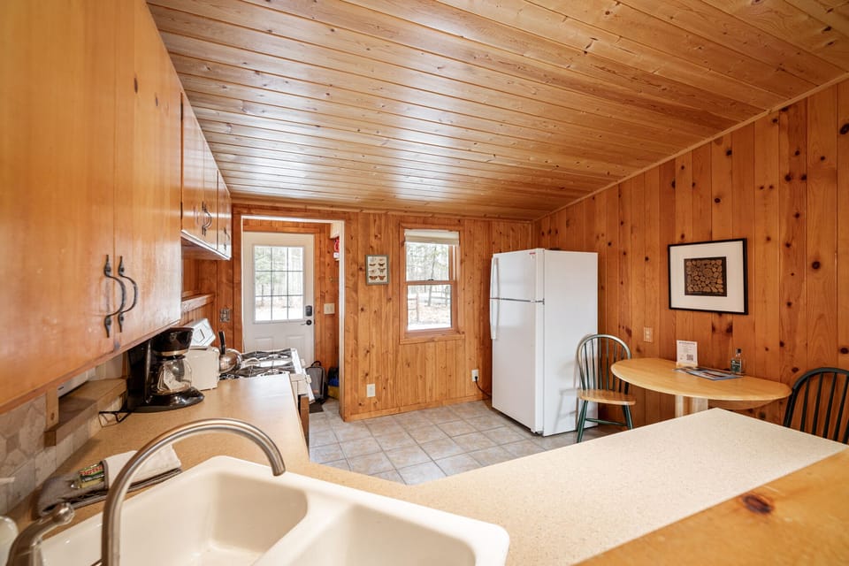 Kitchen view w/ sink, wood cabinetry & natural light streaming through nearby windows.