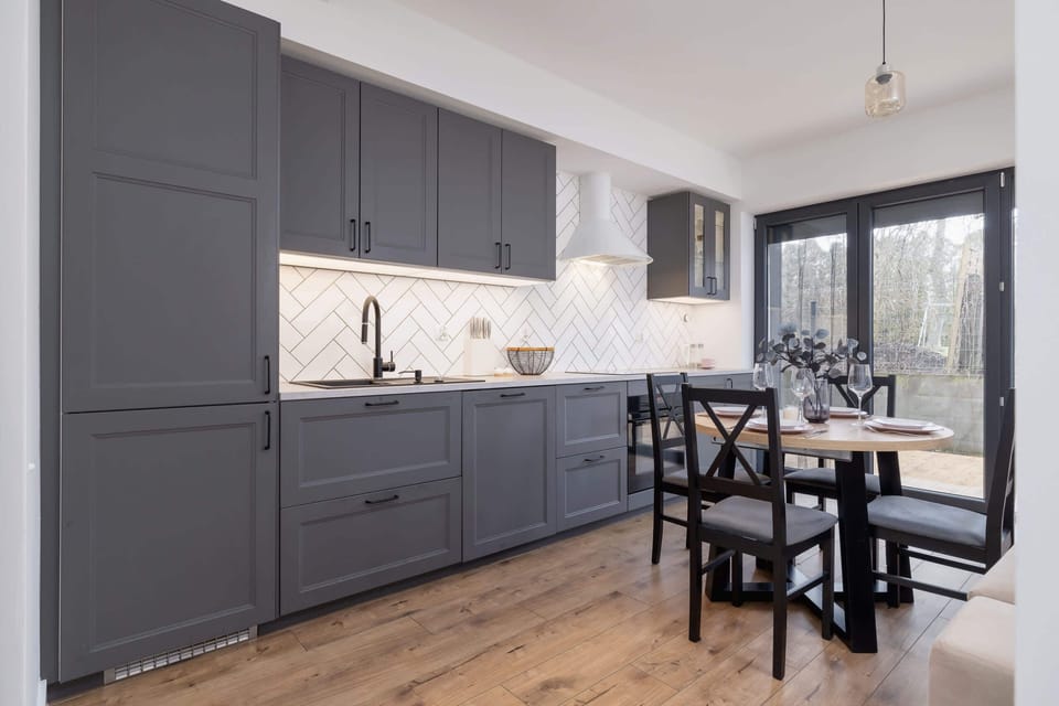 A contemporary kitchen with dark gray cabinets, a sleek black dining table, and large windows offering a view of the outdoor patio.