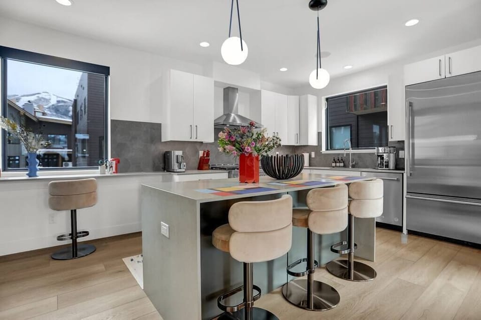 The kitchen strikes a balance with a sleek and modern design, with nods to retro charm. Clean lines and contemporary finishes provide a functional backdrop, while curved, textured barstools and simple round lighting fixtures balance the space.
