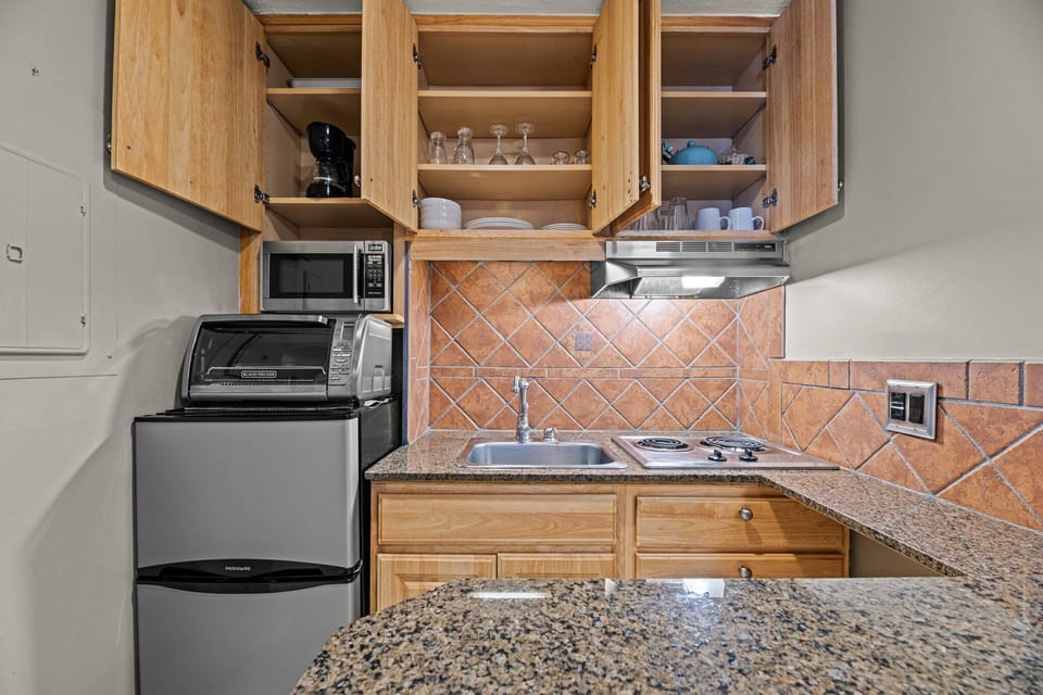Compact culinary haven: stocked with utensils, plates, glasses, and tea kettle.