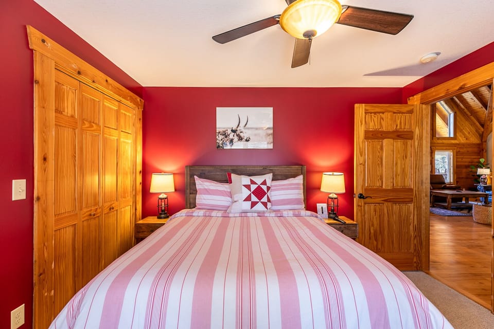 Cozy and colorful, this bedroom at Whiskey River By The New wraps you in warm red tones and rustic pine charm.