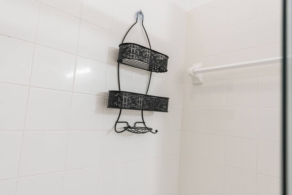 Enjoy this bright and clean bathroom with sleek white tiles and modern black wire shelving, perfect for organizing your essentials while you relax in a refreshing shower.