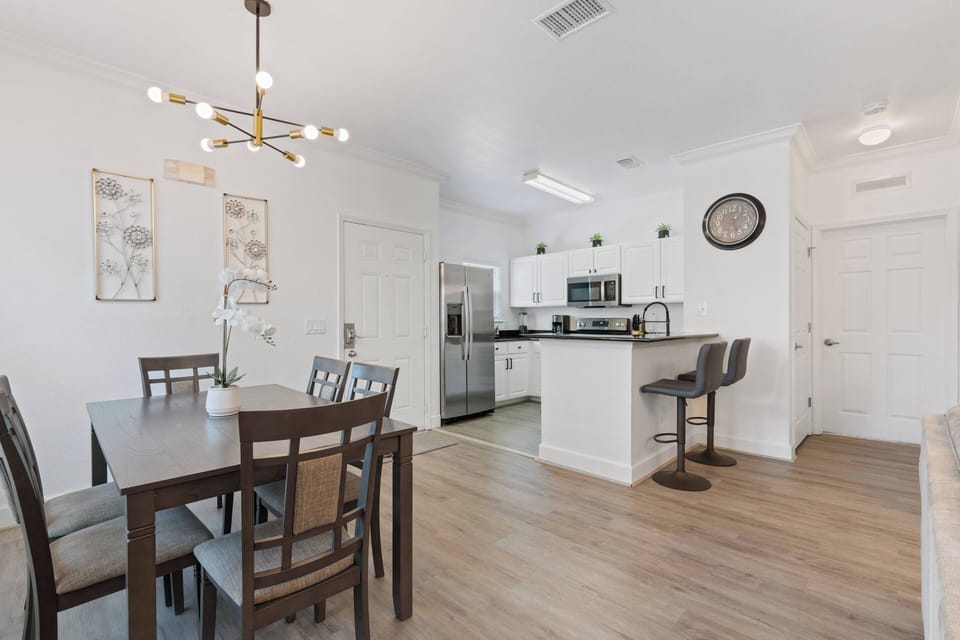 Enjoy meals in this bright dining area with a sleek wooden table and stylish chairs, complemented by a modern kitchen featuring stainless steel appliances and white cabinetry that create a warm, inviting atmosphere.