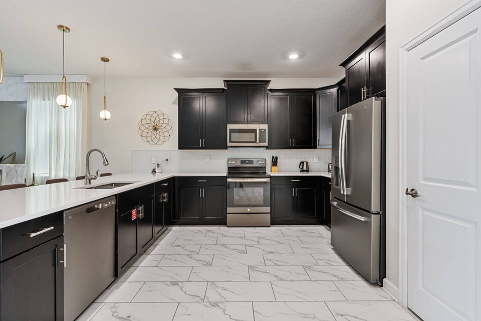Experience a sleek kitchen with dark cabinetry and bright white countertops that beautifully contrast. Enjoy modern stainless steel appliances and elegant pendant lighting that adds a warm ambiance to the space.