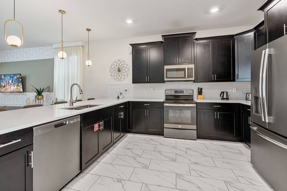 Welcome to this stylish kitchen featuring sleek black cabinets and white countertops for a chic vibe. The polished marble flooring adds sophistication, while modern pendant lights warmly illuminate your culinary adventures.