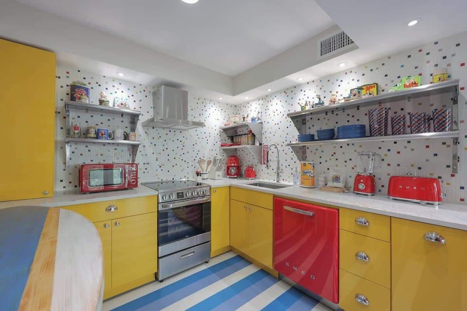 Sunny, retro kitchen with bright yellow cabinets, Smeg appliances, and blue-and-white striped floors.