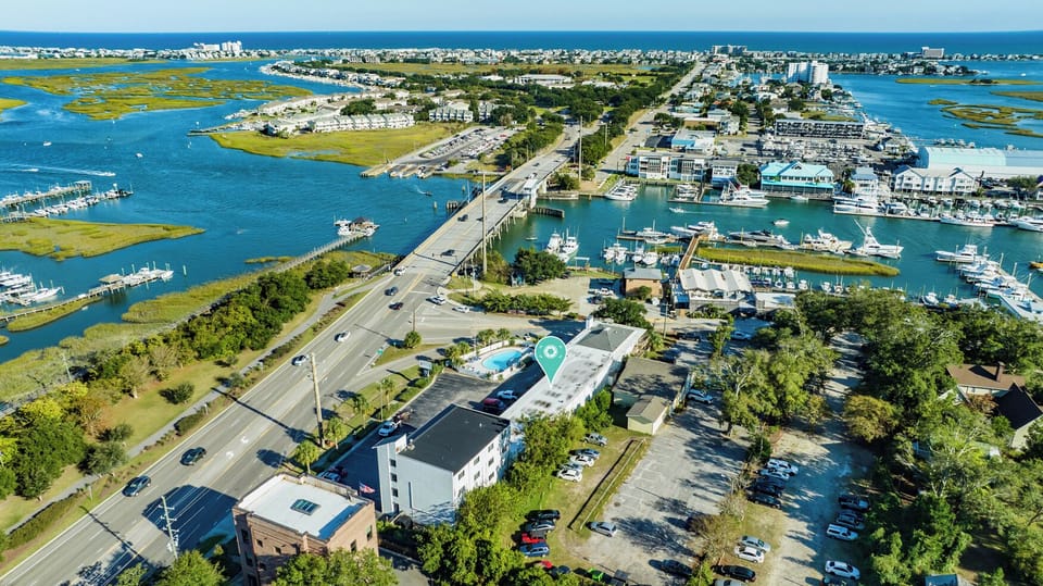 Aerial view of the property nestled along a scenic coastal waterway with marinas, bridges, and vibrant marshlands defining the surrounding landscape.