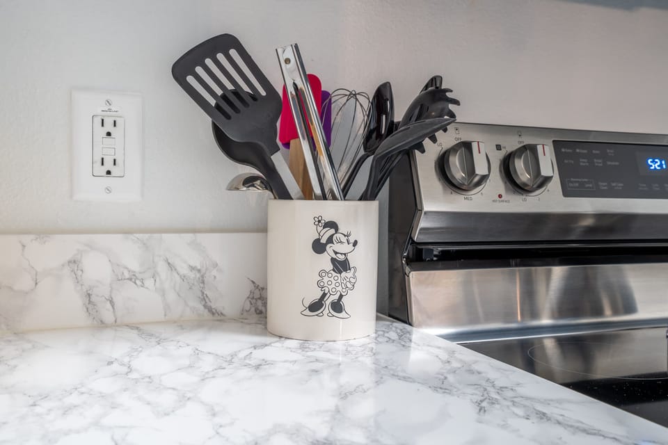 Kitchen utensils organized in a Minnie Mouse holder next to a stainless steel stove on a marble countertop