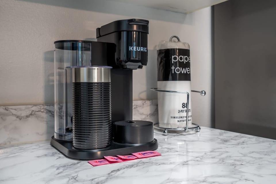 Modern keurig coffee maker on a marble countertop with sweetener packets and paper towels nearby