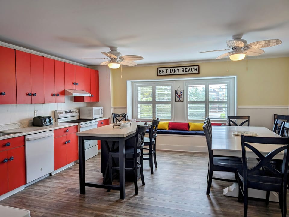 45A Atlantic Ave Unit U6 - Bethany Beach - diining - Perspective of the dining area showing the window seating, ceiling fans, and red kitchen accents.