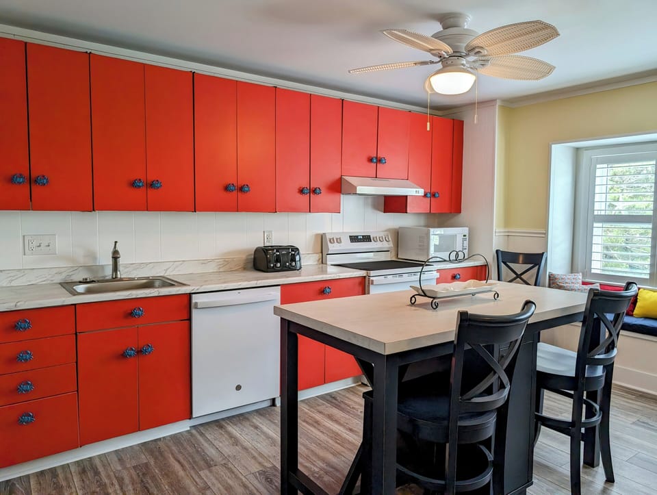 45A Atlantic Ave Unit U6 - Bethany Beach - kithcen overview - Perspective of the kitchen featuring vibrant red cabinetry, white countertops, and a central island with seating.