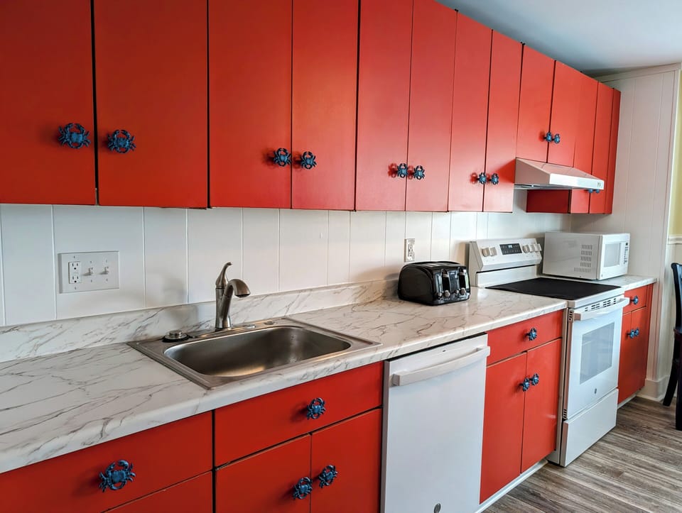 45A Atlantic Ave Unit U6 - Bethany Beach - kitchen - Close-up of the kitchen workspace featuring red lower and upper cabinets, white countertops, and a white dishwasher.