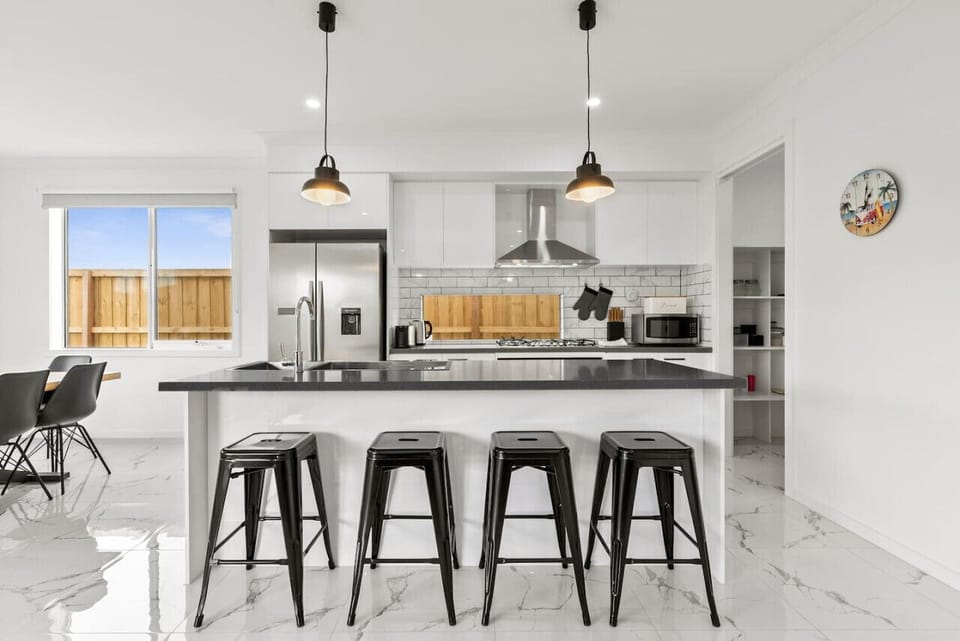 Whip up a feast in this sleek, fully-equipped kitchen featuring a large island with bar seating, stainless steel appliances, pendant lighting, and stylish subway tile splashback