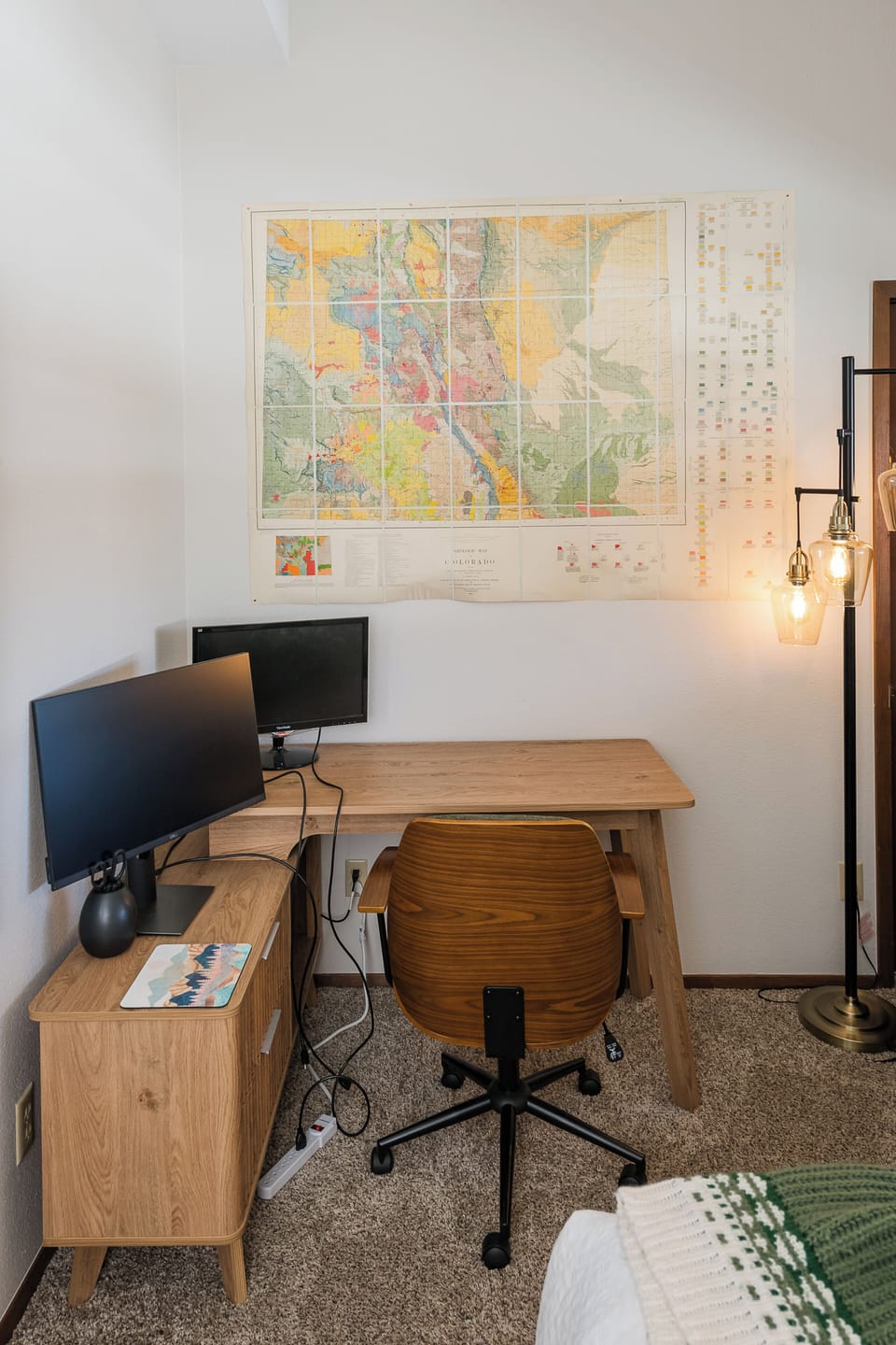 Your dedicated workspace features dual monitors and warm lighting, perfect for remote work with inspiring maps adorning the walls.