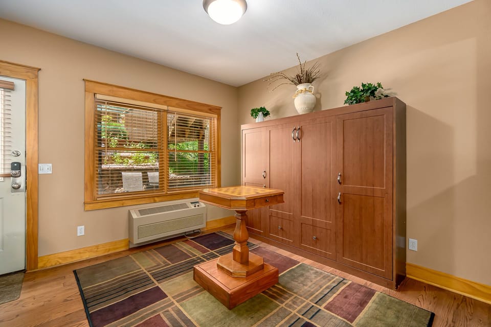 Chess table in the main living area. Armoire along the wall. Window AC unit underneath window.