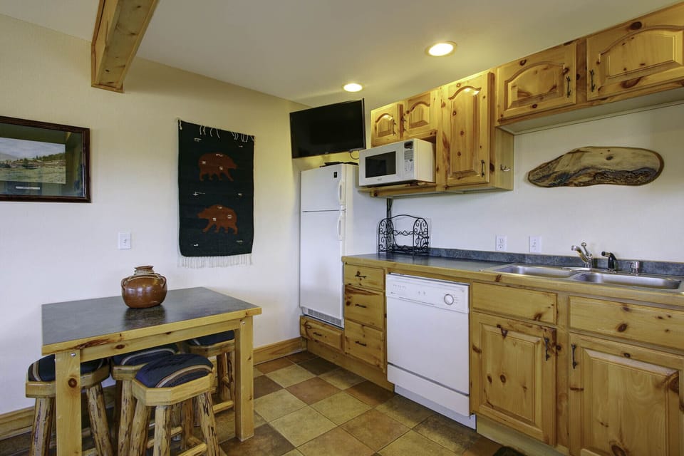 Combo kitchen/dining area. Log table with seating for four. Flat-screen TV above compact refrigerator and freezer. Microwave and dishwasher.