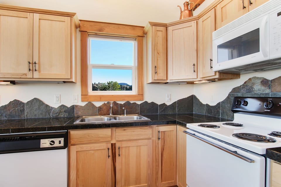 Beautiful mountain skyline backsplash along the granite countertops. Full kitchen has oven, stovetop, dishwasher and microwave.