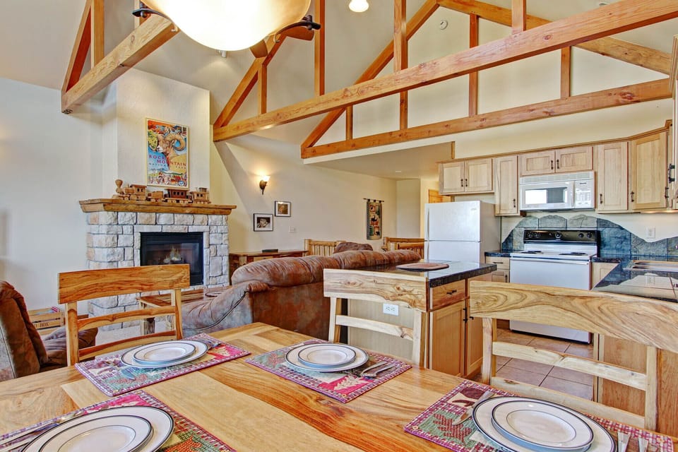 Dining table is adjacent to the living area with its stone fireplace, TV, and sofa seating. Gorgeous mountain views can be enjoyed from both. 