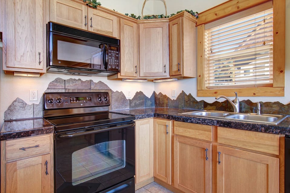 Beautifully decorated full kitchen. Mountain-themed granite backsplash along countertops. Full size refrigerator, dishwasher, oven, stovetop, and microwave.