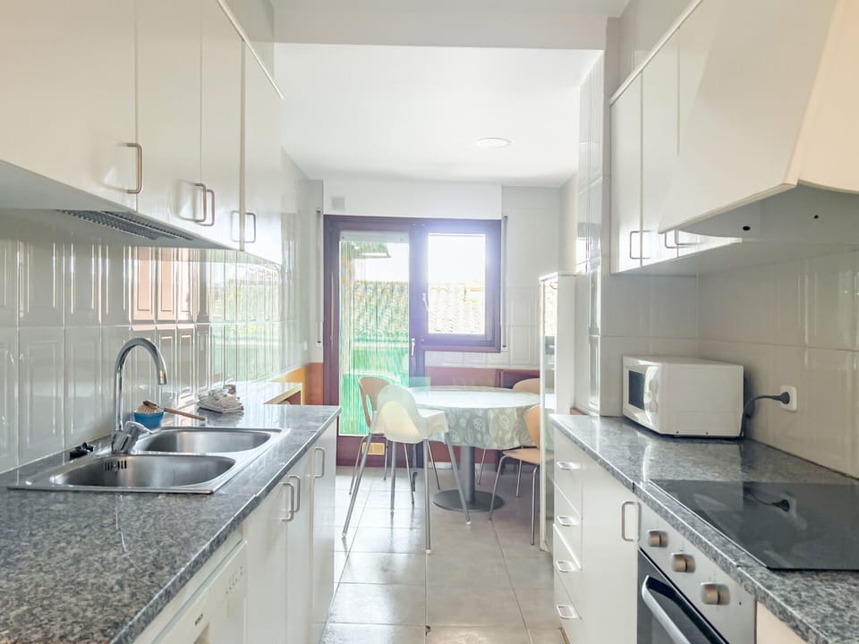 This bright kitchen in a Banyoles apartment features modern appliances, sleek white cabinets, and a cozy dining space. Large windows fill the room with natural light, creating a welcoming atmosphere for cooking and sharing meals.