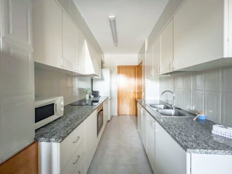 This modern and functional kitchen in a Banyoles apartment offers sleek white cabinetry, granite countertops, and essential appliances. The practical layout includes a double sink, ample storage, and efficient lighting for a comfortable cooking experience.