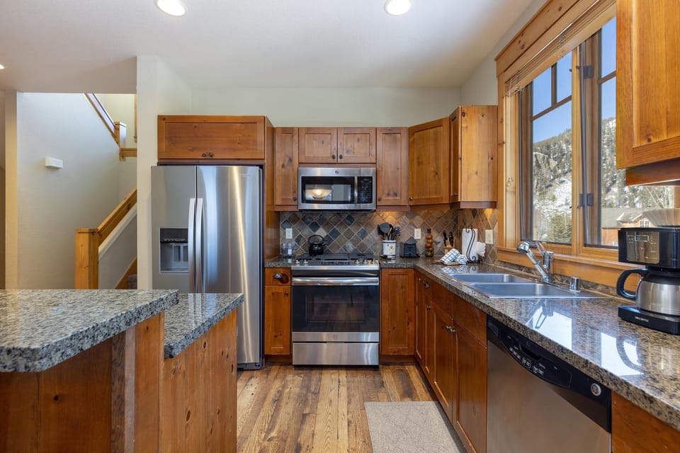 Modern kitchen with wooden cabinets, granite countertops, stainless steel appliances, including a refrigerator, oven, and microwave. A window above the sink provides natural light.