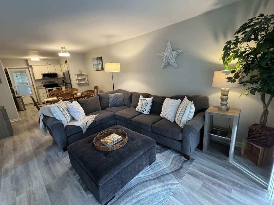 The open-concept living space features light grey walls and durable wood-look flooring. 