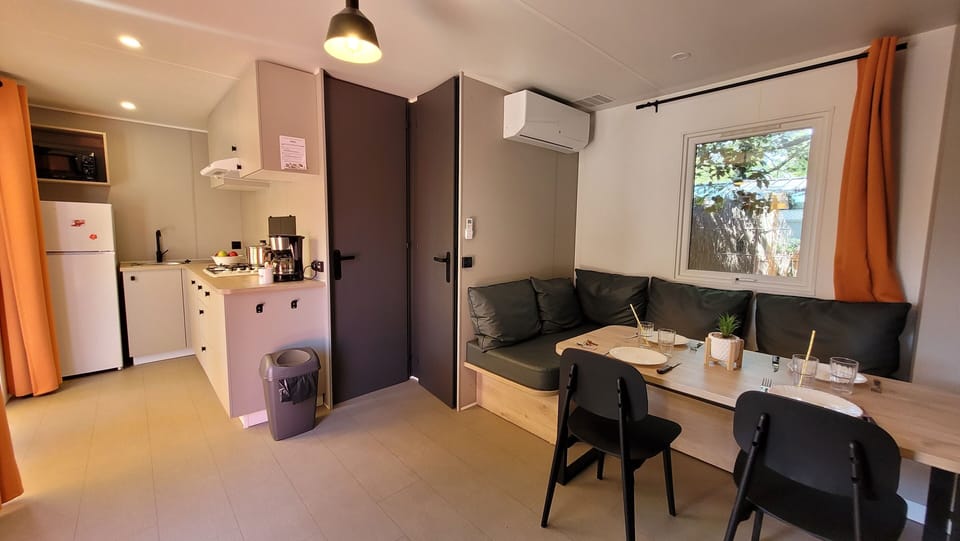 A stylish and spacious 28 m² mobile home interior at Camping L’Orée du Bois, featuring an inviting kitchen and a cozy dining area with ample seating.