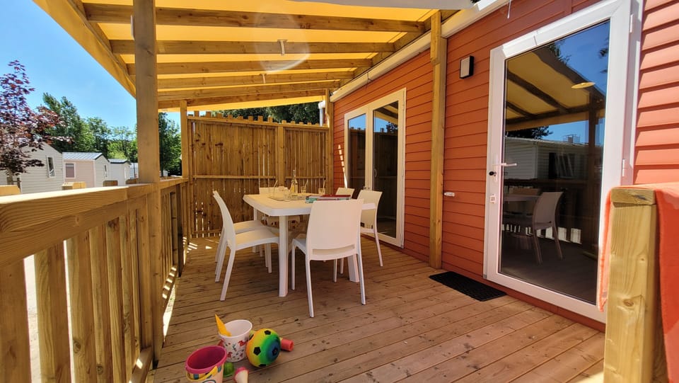 The shaded terrace provides a delightful setting for meals, furnished with a dining table, while being surrounded by a lush green environment.