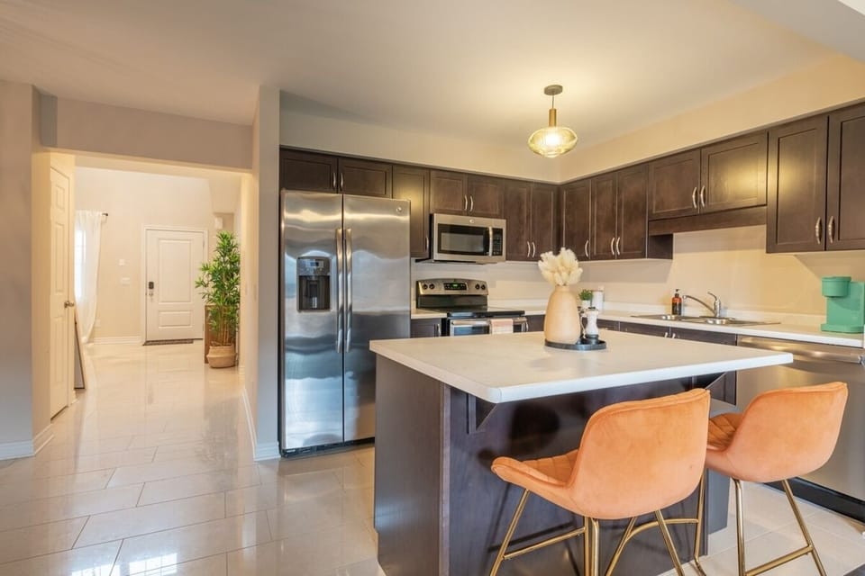 Modern kitchen with stainless steel appliances, dark wood cabinetry, and a spacious island. Bright lighting complements the open, airy design, while the stylish bar stools add a touch of warmth. Perfect for cooking and gathering with loved ones!