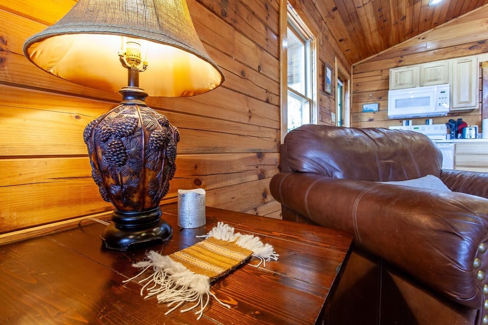 Table lamp and leather seating accent the open great room with tongue-and-groove wood walls and mountain cabin character. The open layout connects the living space to the rest of the cabin interior.