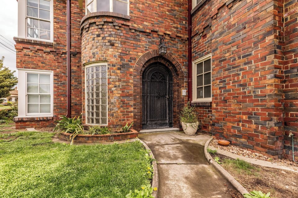 EXTERIOR: A charming brick archway leads to the front door, framed by lush greenery