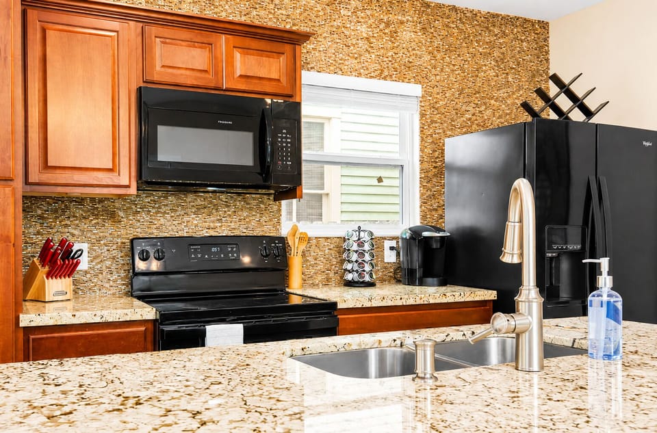 Fully equipped kitchen featuring granite counters, double sink, refrigerator, electric range, microwave, coffee maker and warm wood cabinetry.